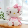 Gấu bông Kitty váy caro nơ hồng ngồi cạnh cửa sổ, má hồng nhẹ, dáng ngồi đáng yêu