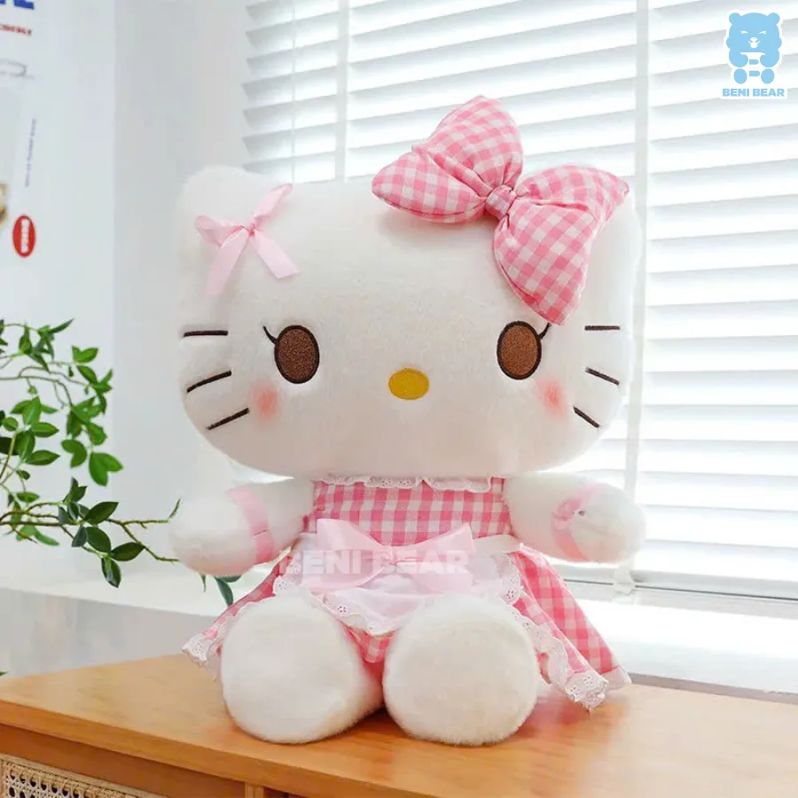 Gấu bông Kitty váy caro nơ hồng ngồi cạnh cửa sổ, má hồng nhẹ, dáng ngồi đáng yêu