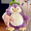 Gấu bông cánh cụt cà tím được ôm với biểu cảm ngơ đáng yêu, chân vàng nhạt xinh xắn